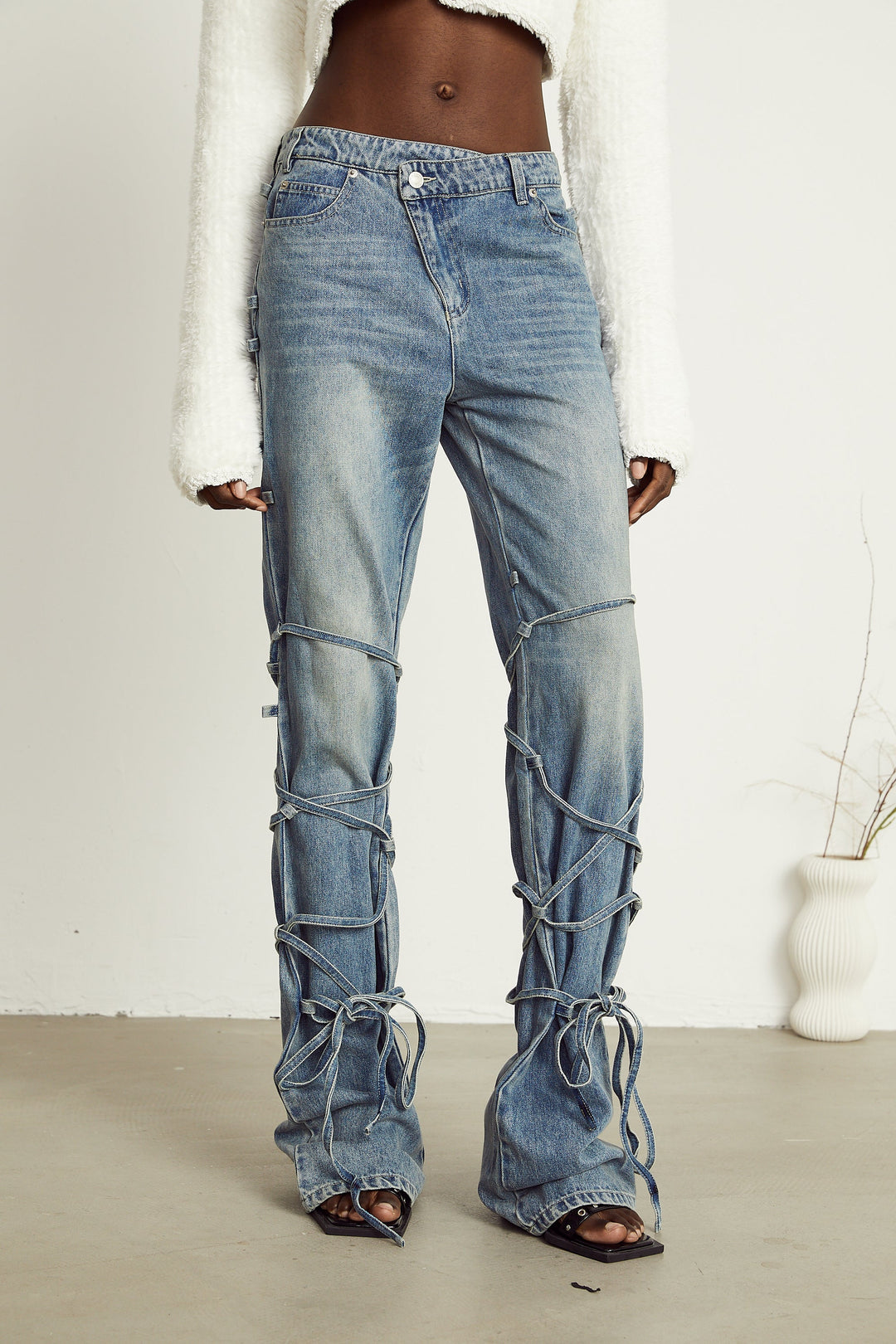 Light wash blue jeans with layered strap details and tie-up cuffs on the lower leg