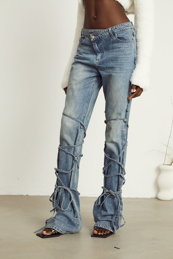 Light wash blue jeans with layered strap details and tie-up cuffs on the lower leg