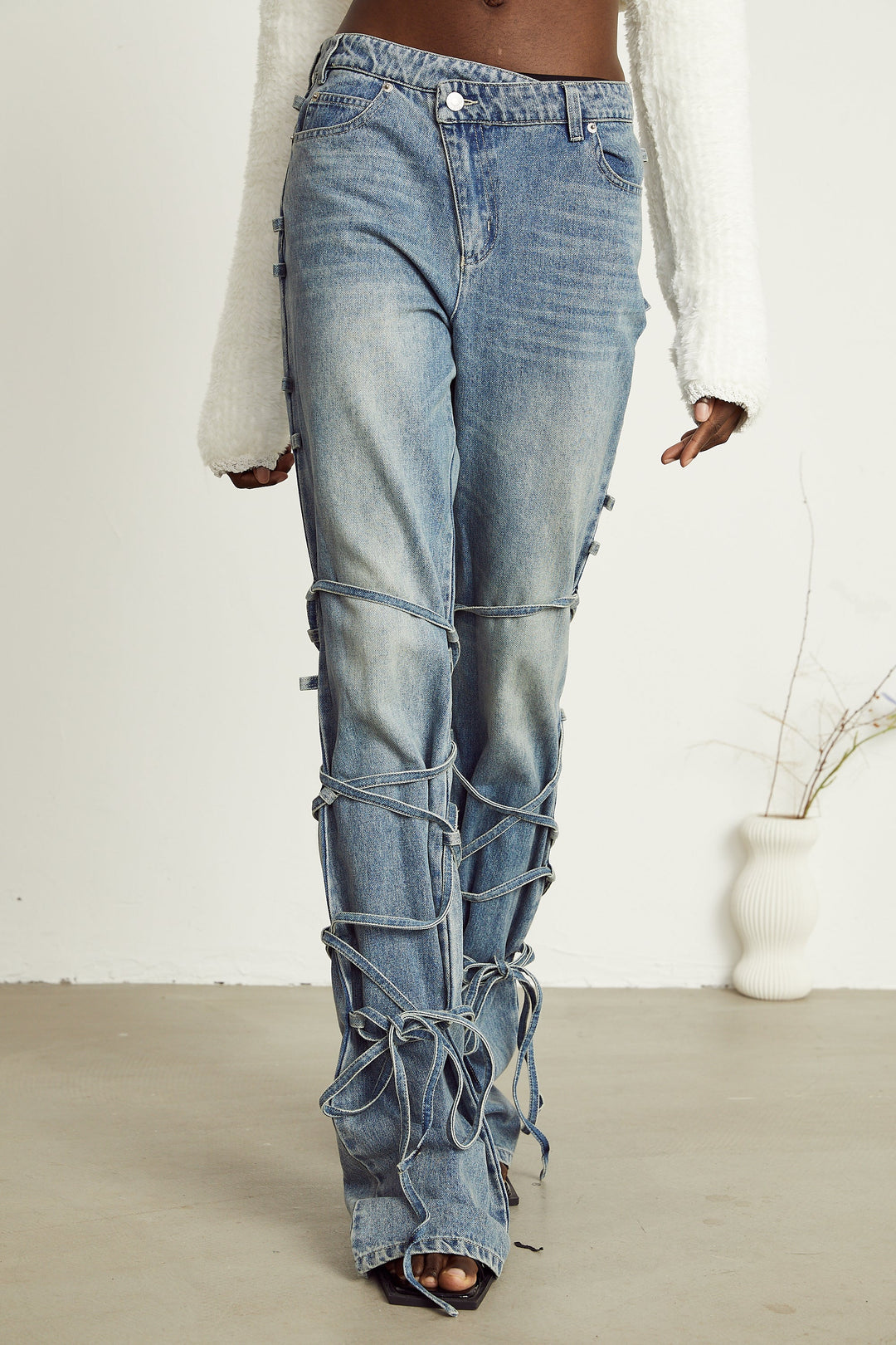 Light wash blue jeans with layered strap details and tie-up cuffs on the lower leg