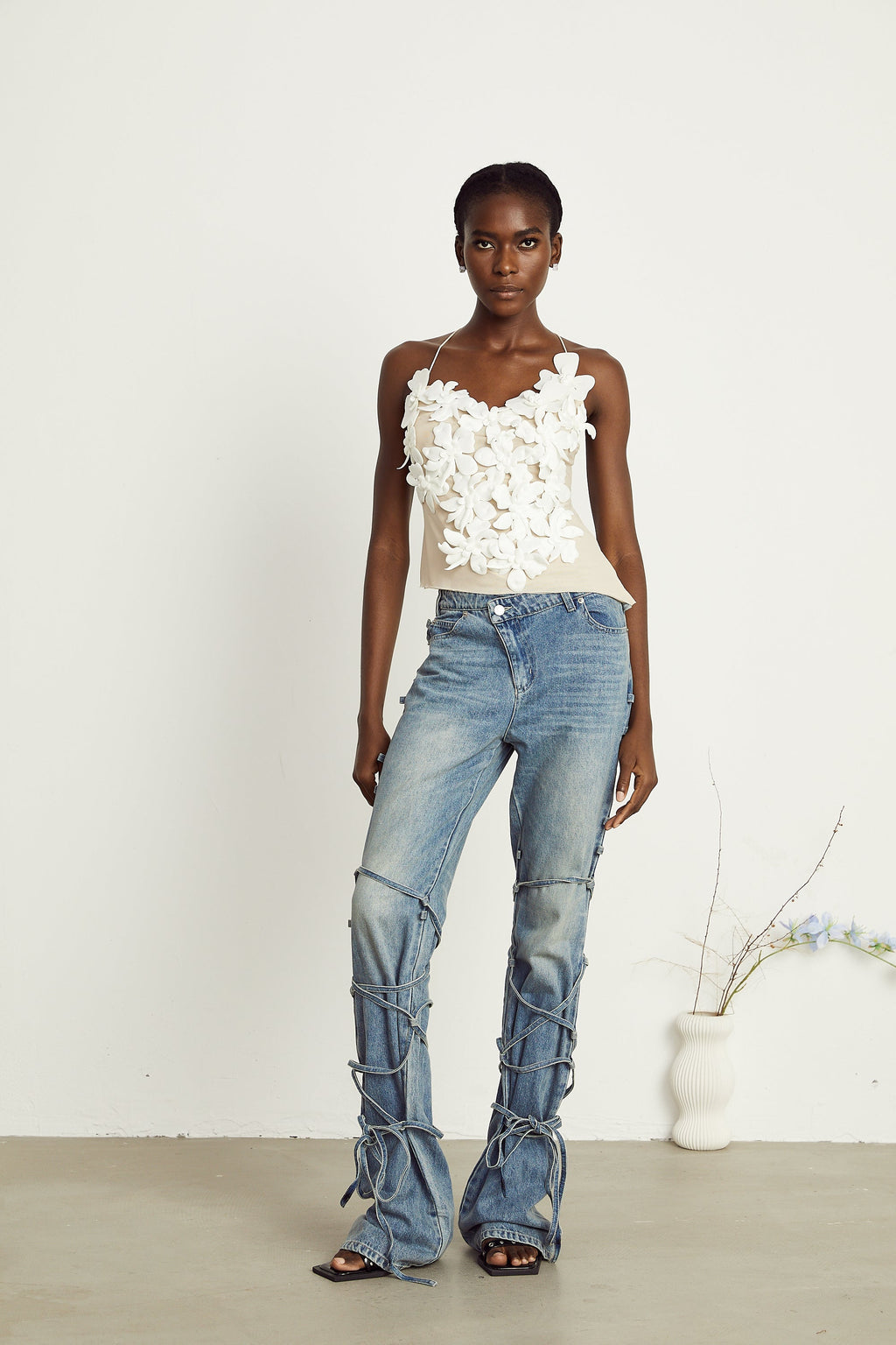 Light wash blue jeans with layered strap details and tie-up cuffs on the lower leg