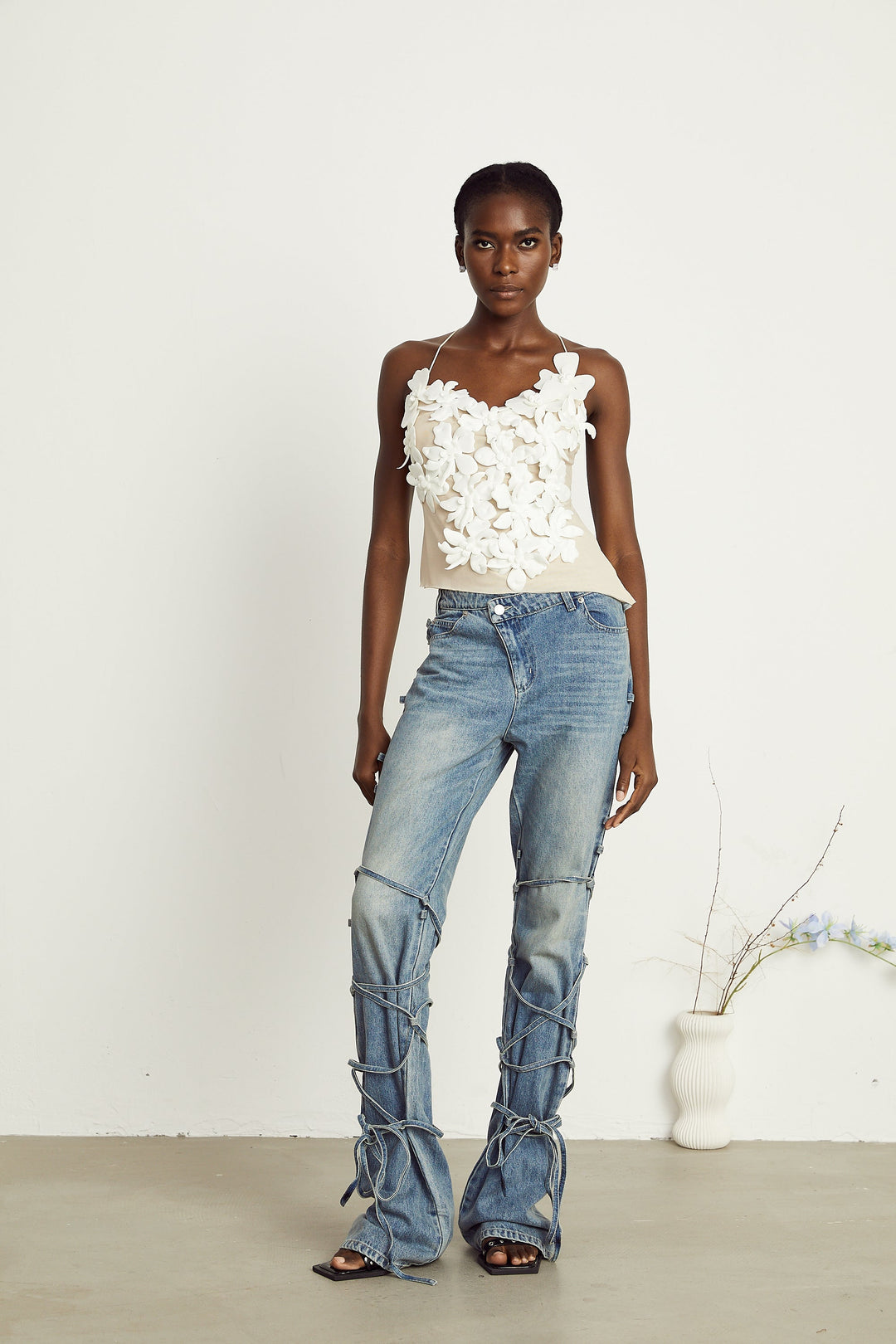 Light wash blue jeans with layered strap details and tie-up cuffs on the lower leg
