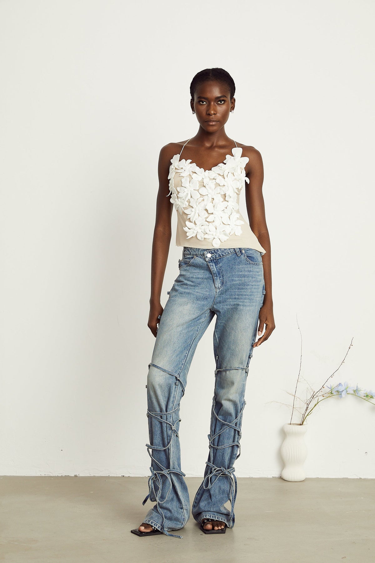 Light wash blue jeans with layered strap details and tie-up cuffs on the lower leg