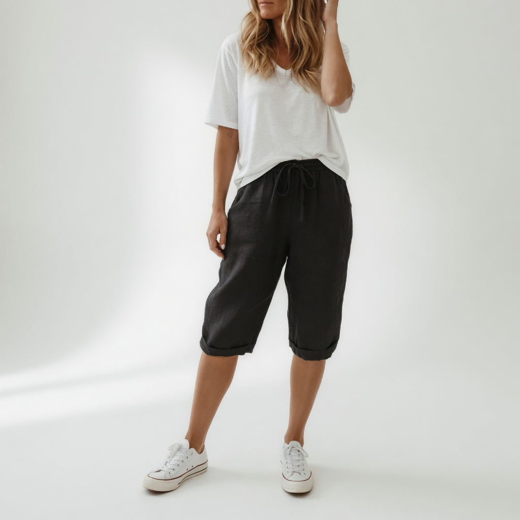 Woman wearing beige bermuda shorts with drawstring waist and rolled cuff hem, paired with a white t-shirt and white sneakers
