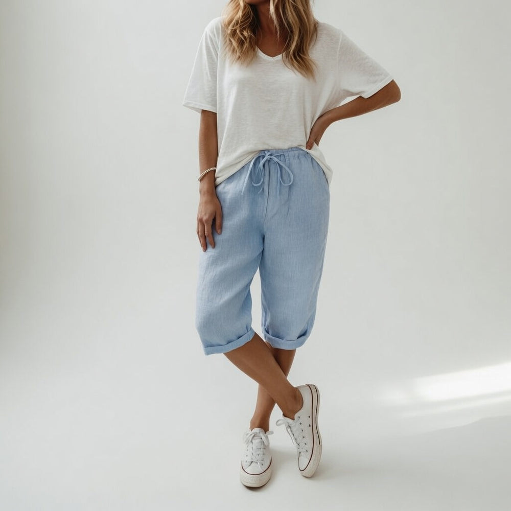 Woman wearing beige bermuda shorts with drawstring waist and rolled cuff hem, paired with a white t-shirt and white sneakers