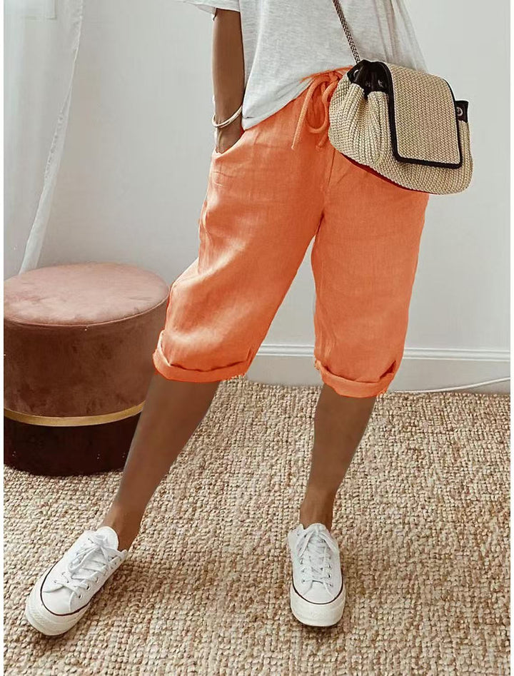 Women's beige bermuda shorts with cuffed hems and drawstring waist, paired with white t-shirt and white sneakers