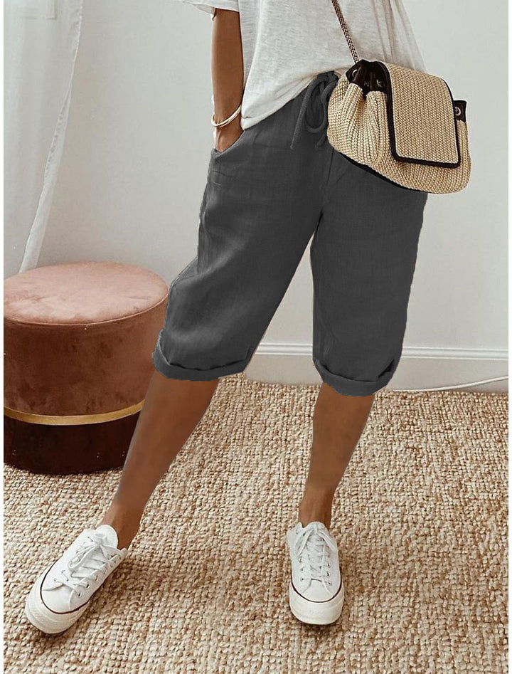 Women's beige bermuda shorts with cuffed hems and drawstring waist, paired with white t-shirt and white sneakers