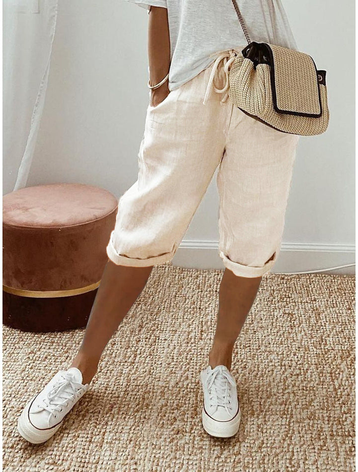 Woman wearing beige bermuda shorts with drawstring waist and rolled cuff hem, paired with a white t-shirt and white sneakers