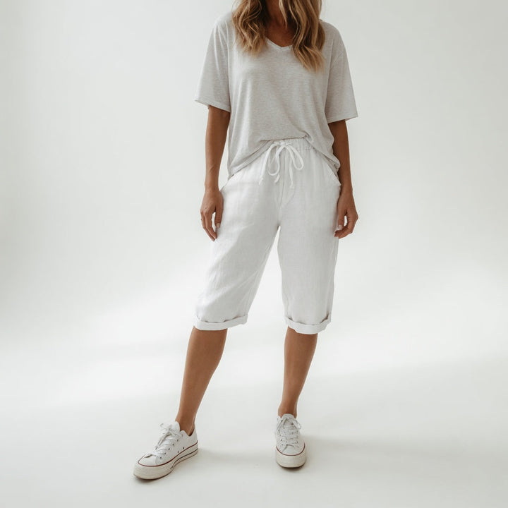 Woman wearing beige bermuda shorts with drawstring waist and rolled cuff hem, paired with a white t-shirt and white sneakers