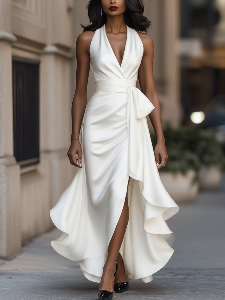 Woman wearing a halterneck maxi dress with a tie waist, high split and cascading ruffle hem