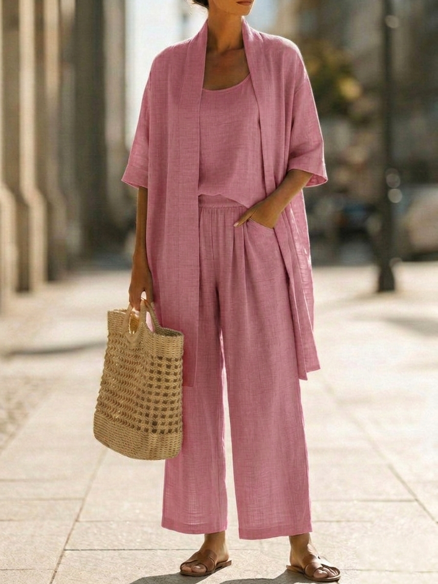 Woman wearing white three-piece set with open cardigan, scoop-neck top and wide-leg trousers, holding woven tote bag